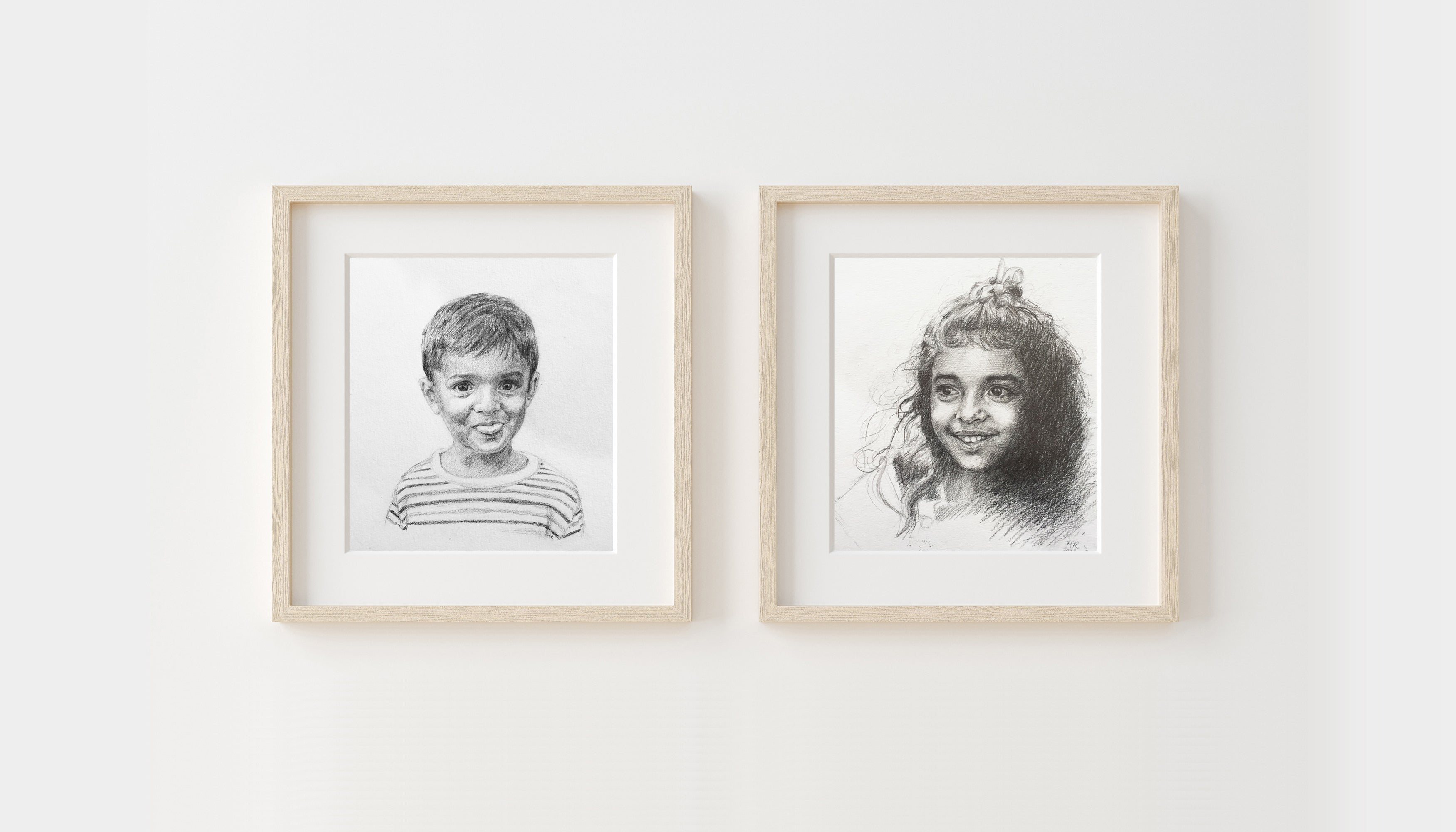 Two framed black and white pencil portraits of a boy pulling a face and a girl on a white wall.